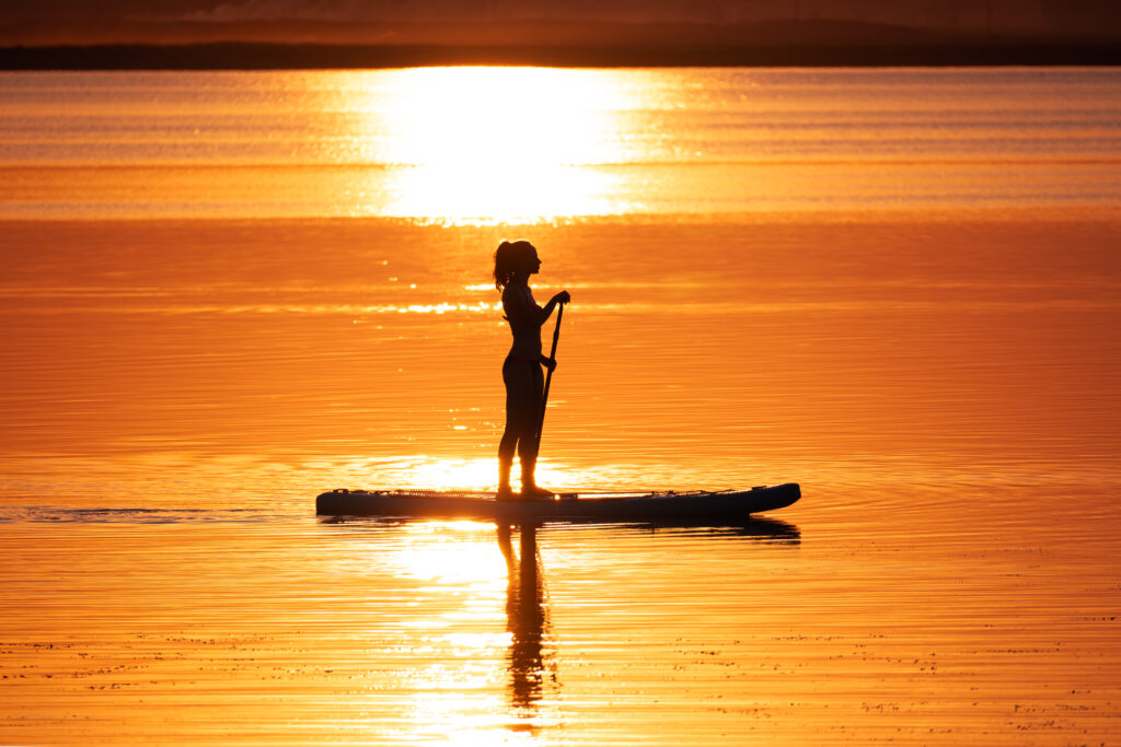 a young woman stands on a board with a paddle and swims on a beautiful lake. Girl on sup board with beautiful colored sunrise background